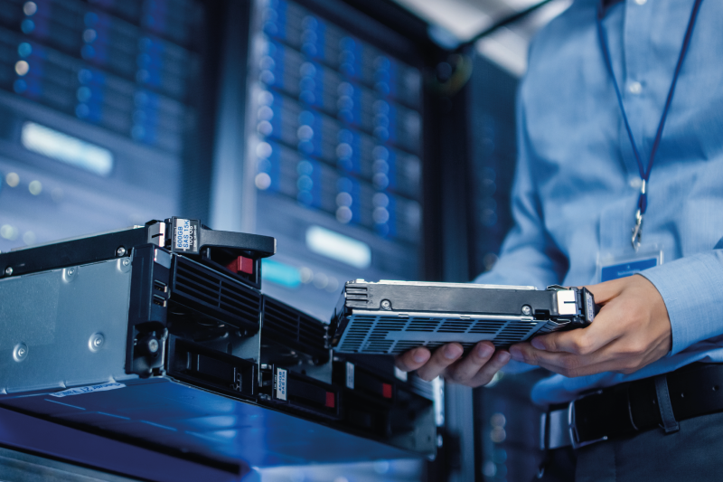 Man in blue shirt holding hard drive in server room