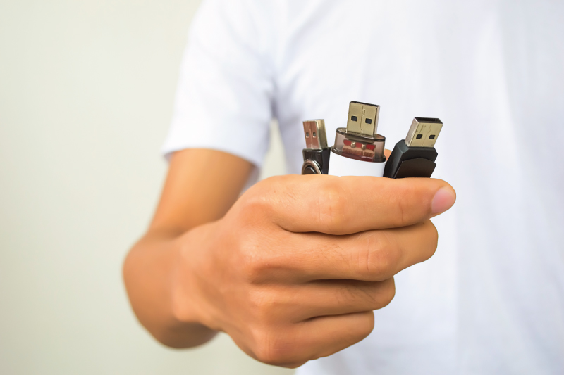 person in white shirt holding 3 USB flash drives in hand