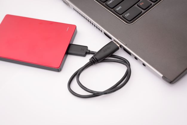 External hard drive plugged into laptop USB port with cord connecting them
