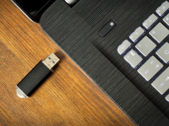 Black USB flash drive and black laptop next to eachother on wood table