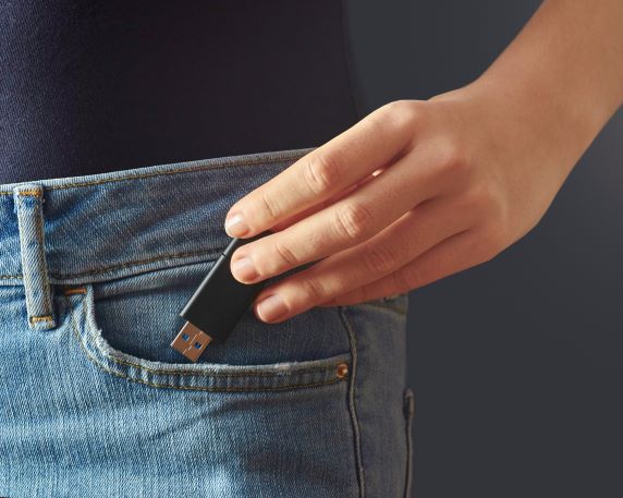 Person placing black USB flash drive in jean front pocket