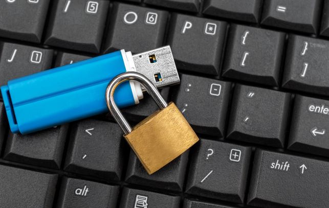 blue USB flash drive sitting on black keyboard next to gold lock