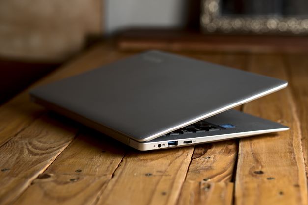 Silver laptop partially opened with drive ports showing sitting on wood table